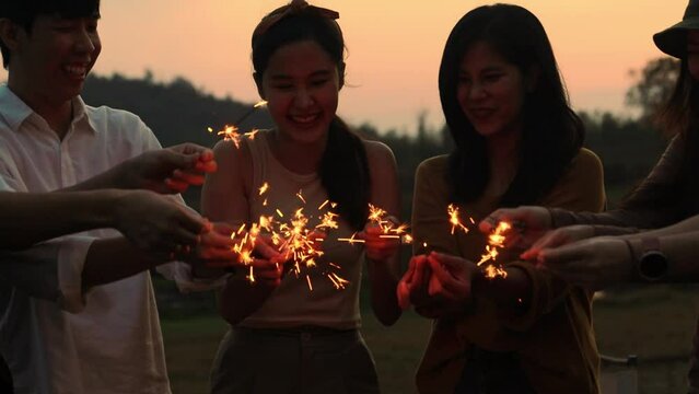 Friendly group of asian men and women doing recreational activities having fun singing dancing having fun setting fire to fireworks evening with beautiful sparks travel day camping trip holiday.