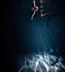Fototapeta na wymiar Underwater shoot of beautiful pregnant woman swimming in water through sunbeams.