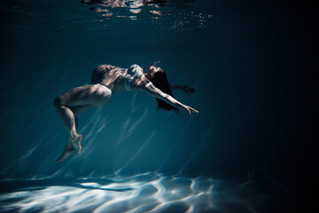 Underwater shoot of beautiful pregnant woman swimming in water through sunbeams.
