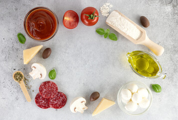 Ingredients for cooking pizza: mozzarella, onion, tomato, flour, mushrooms, salami, spices, olives on a gray background. Top view. Copy Space.