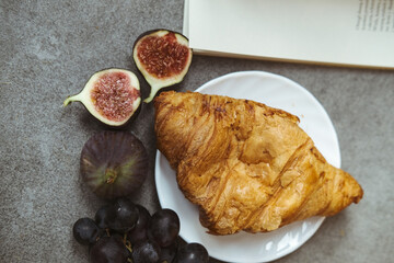 Autumn attributes. Croissant, dark grapes, book and figs on the grey table. Gold October