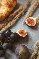 Autumn attributes. Croissant, dark grapes, book and figs on the grey table. Gold October
