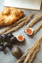 Autumn attributes. Croissant, dark grapes, book and figs on the grey table. Gold October