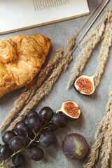 Autumn attributes. Croissant, dark grapes, book and figs on the grey table. Gold October