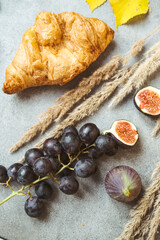 Autumn attributes. Croissant, dark grapes, book and figs on the grey table. Gold October