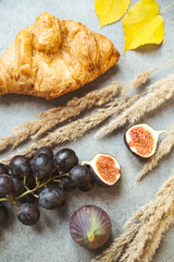 Autumn attributes. Croissant, dark grapes, book and figs on the grey table. Gold October