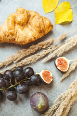 Autumn attributes. Croissant, dark grapes, book and figs on the grey table. Gold October