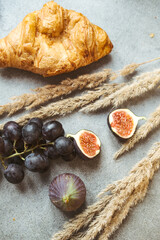 Autumn attributes. Croissant, dark grapes, book and figs on the grey table. Gold October