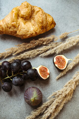 Autumn attributes. Croissant, dark grapes, book and figs on the grey table. Gold October