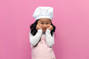 little Asian girl in chef uniform is sad and bored on pink background, Korean child cook is unhappy