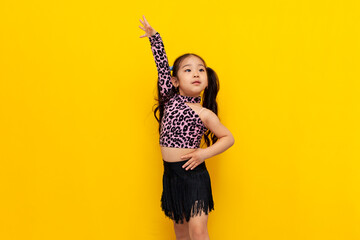 little asian girl in dance outfit dances chachacha on yellow isolated background, korean child dancer trains dance