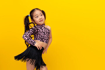 little asian girl in dance outfit dances chachacha on yellow isolated background, korean child...