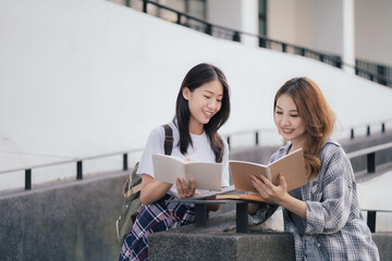 Asian college student reading a book study on laptop prepare for the exam Or work on a group project while sitting on the steps of the university.