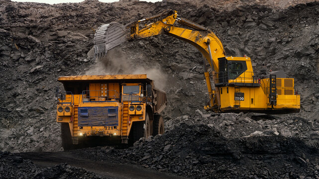 A huge excavator loads rock formation into the back of a heavy mining dump truck. Open pit coal mining.