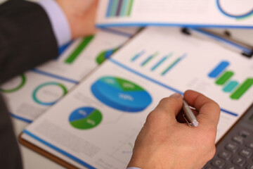 Businessman is holding pen and pointing to marketing chart and is working with financial documents....