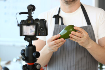 Chef blogger holding avocado gives some cooking tips for vlog at home. Remote cooking classes...