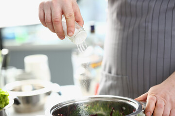 Cook pours salt and water into saucepan. Dosage of salt in dishes cooking