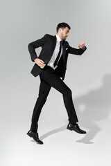 full length of businessman in stylish suit checking time and levitating on grey background.