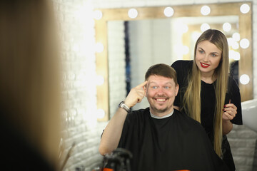 Male client communicates with female hairdresser in beauty salon. Man pointing finger at hair sitting in barbershop
