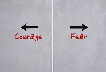 Cement wall with text and opposite direction to COURAGE or FEAR, choices to be brave and overcome...