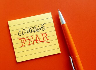 Note on orange background with orange pen writing COURAGE over FEAR , means to move from fear to...