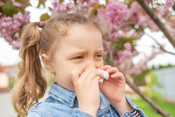 The child wipes his nose with a napkin. Seasonal allergy to flowers.