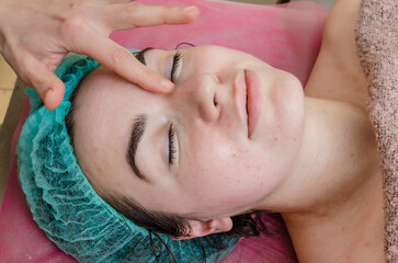 Top view of female face in cosmetic cap. The client is waiting for the pleasure of facial massage.