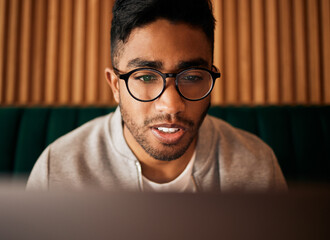 .. Closeup of geeky young indian man wearing glasses while reading something interesting and sitting inside. Man wearing glasses while reading online. Dedicated male student doing research in cafe.