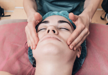 Cheek massage. A woman's face in a cosmetic cap and the hands of a beautician. Cosmetic procedures.