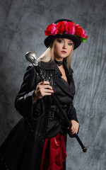 Fototapeta premium A pretentious Gothic lady in a long leather coat and a hat with roses, uses a cane.