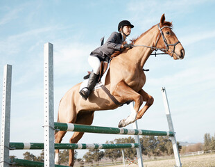 Over we go. Full length shot of a young female rider jumping over a hurdle on her horse.