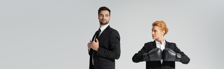 haughty businessman and purposeful businesswoman in boxing gloves looking at each other isolated on...