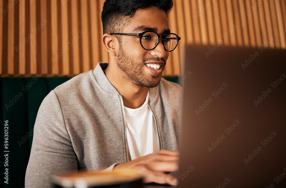 Poster .. Handsome indian man with glasses sitting alone and using laptop in cafe. Man using wifi to browse the internet or doing freelance work in a cafe. Male student doing research on internet.
