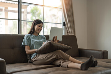 Obraz premium woman smiling and using laptop computer at home comfortably in living room. Smart working female people notebook. Surfing the web. Enjoying technology and connection