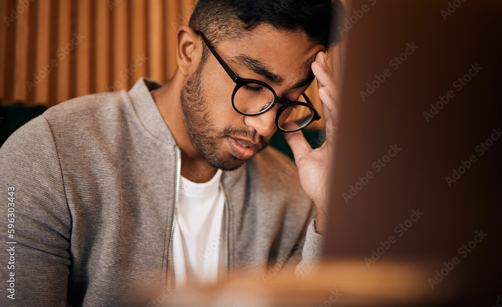 Poster young stressed indian man or student struggling with headache while browsing on a laptop in a cafe. 