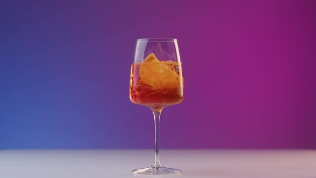 Bartender drops a slice of orange into glass with cold summer cocktail with a beautiful movement. Final action serving an aperol cocktail at party. Wonderful refreshing cocktail on neon bar lighting