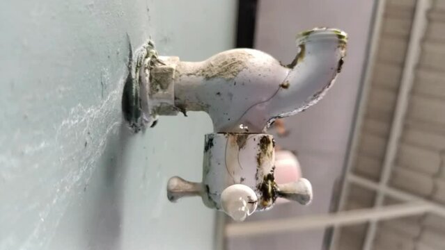 Water drips from an old faucet in bathroom, close-up. Dripping water faucet valve. Drops of water fall from faucet. Old plumbing is covered with rust and limestone deposits. saving water.