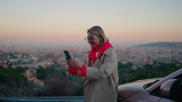 Caucasian smiling hipster girl looking at smartphone camera during video call, share experiences and emotions while stands on scenery view background.Female tourist gesturing while talking on cellula