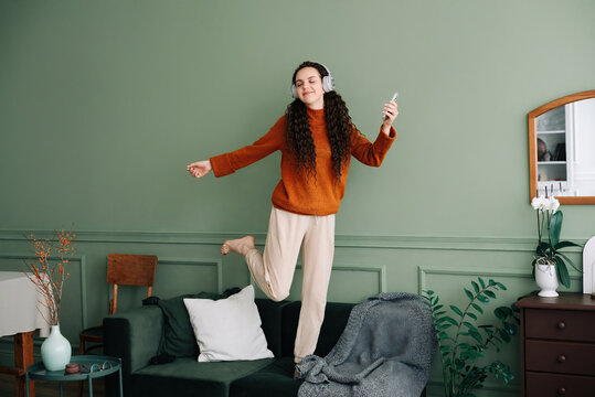 Joyful young woman dancing to her favorite music at home. Happy girl experiencing joy while listening to popular music with headphones. Pretty girl having fun and dancing to music in her living room