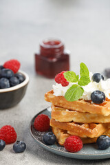 Waffles with berries and whipped cream in a plate on a gray table