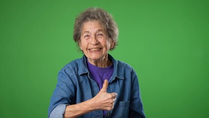 Portrait of excited, surprised elderly senior old woman with wrinkled skin saying WOW smiling giving a thumbs up. Grey hair smiling isolated on green screen background studio