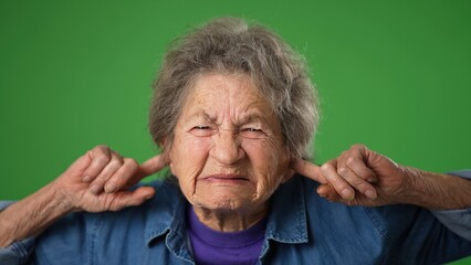 Funny unhappy frustrated sad angry toothless old elderly senior woman with wrinkled skin and grey hair closed eyes cover ears do not want to listen scream isolated on green screen background portrait