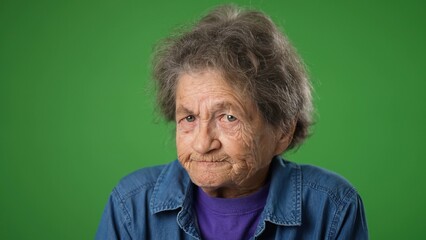 Portrait of toothless, angry upset frustrated elderly senior old woman with wrinkled skin and grey hair on green screen background.