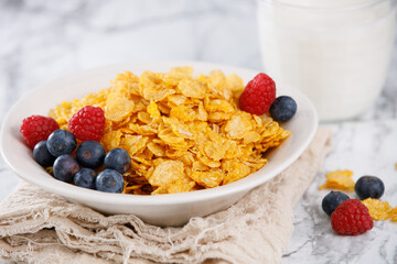 Corn flakes with blueberries and raspberries with milk on a marble table. Quick and healthy breakfast