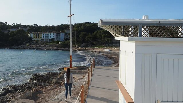 one of the beaches of Illetas, Mallorca, in winter with the sand covered with algae, and things brought by the sea and a young woman walking and stopping to observe the horizon