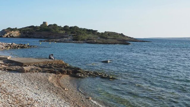 Locality of Illetas you can see part of a virgin beach with sand and rocks and in front of a small islet with an abandoned watchtower