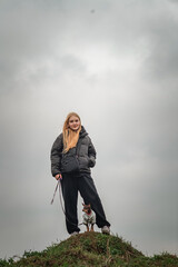 A beautiful young blonde girl walks a purebred Toy Terrier in cloudy weather.