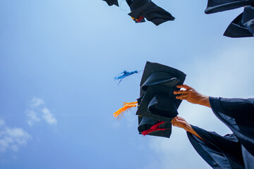 Close-up of graduation ceremony university high school graduates throwing cap on the blue sky. - obrazy, fototapety, plakaty