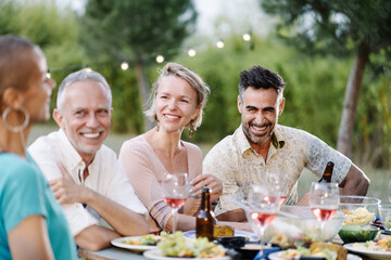 Mature Friends listening to fun conversation at dinner party in the garden in summer