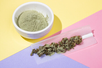 Crushed medical marijuana buds in roll paper sprinkled with kief, filter, green powder in a white...